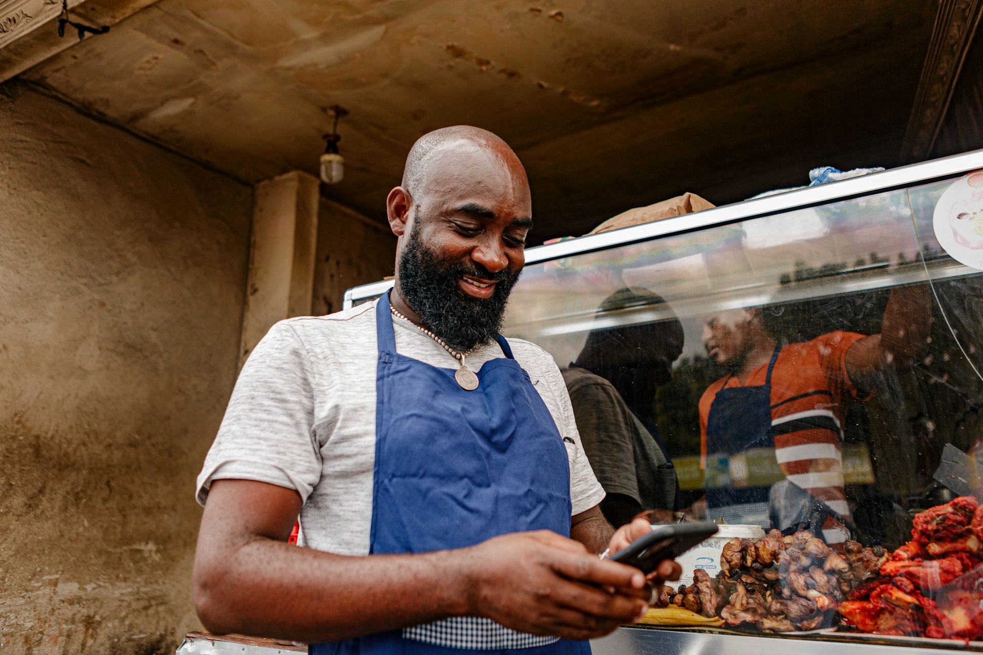 Small business owner in an apron at his shop counter, checking his phone