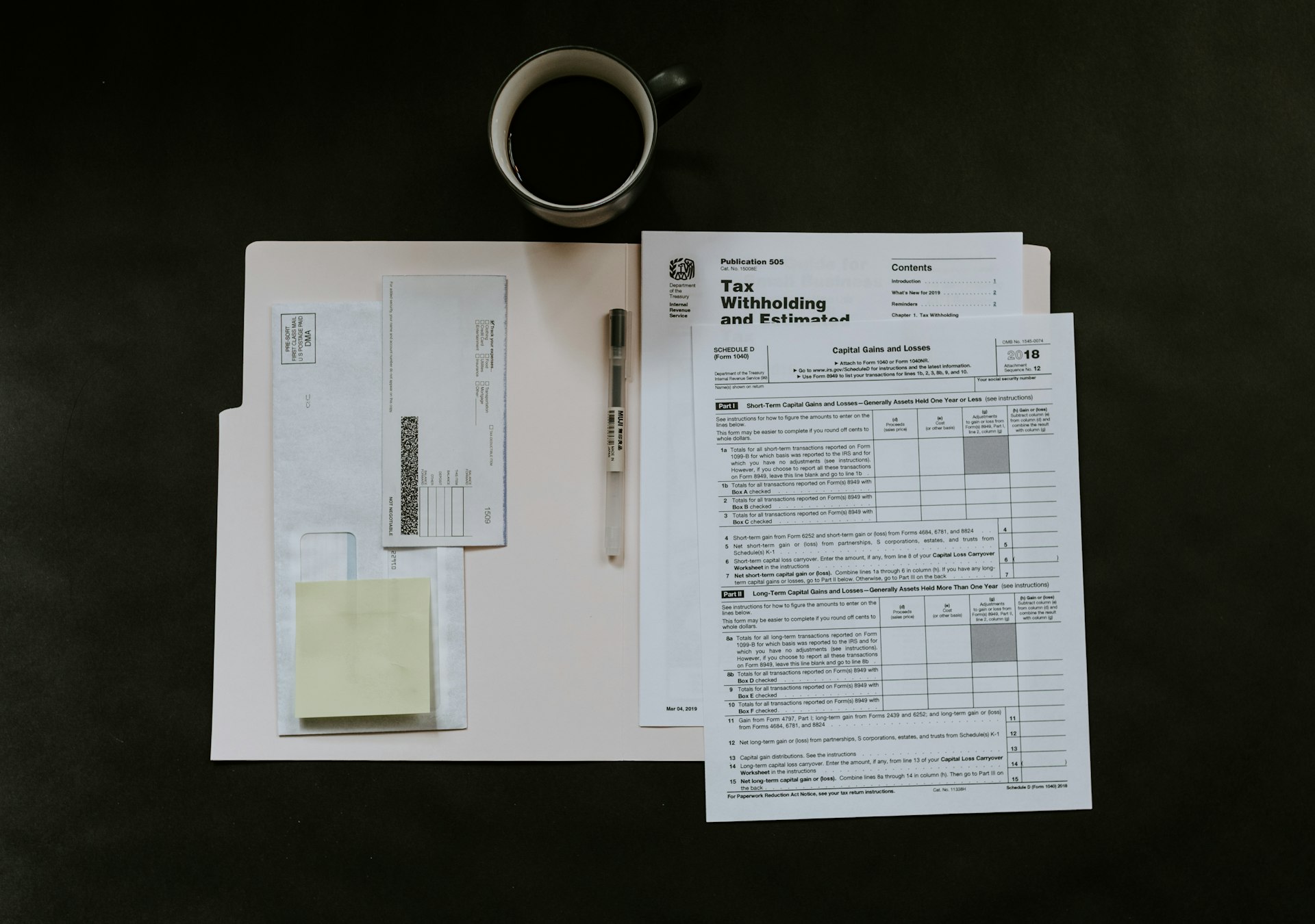Tax forms, a pen and a coffee mug on a dark desk